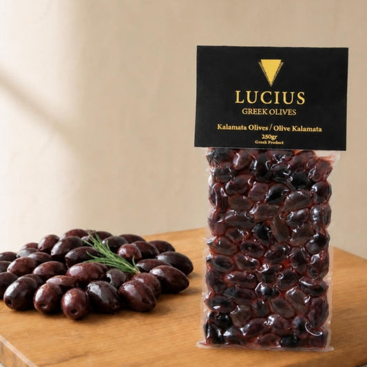 Lucius whole Kalamata olives in a 250g vacuum pouch beside a pile of olives on an oak board