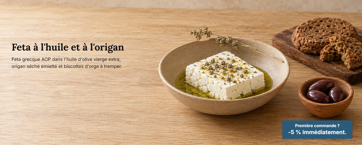 Feta dans un bol peu profond avec de l'huile d'olive et de l'origan séché émietté, des biscottes d'orge et des olives sur une table en chêne