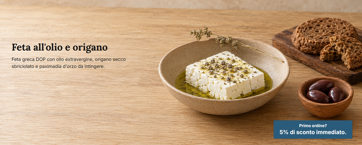 Feta in una ciotola bassa con olio d'oliva e origano secco sbriciolato, paximadia d'orzo e olive su un tavolo di rovere