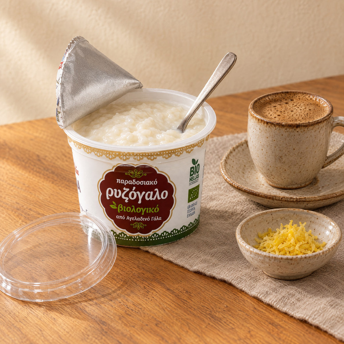 Ein geöffneter Becher Gaitanidis Rizogalo mit Löffel, ein griechischer Kaffee und geriebene Zitronenschale