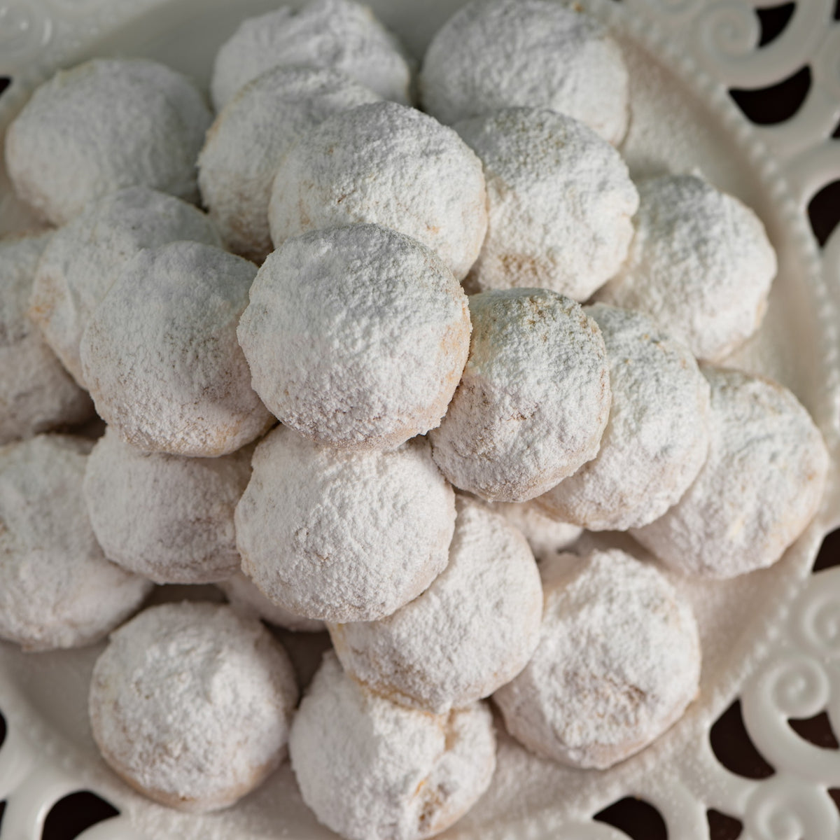 Gros plan de kourabiedes enrobés de sucre glace sur une assiette blanche ajourée