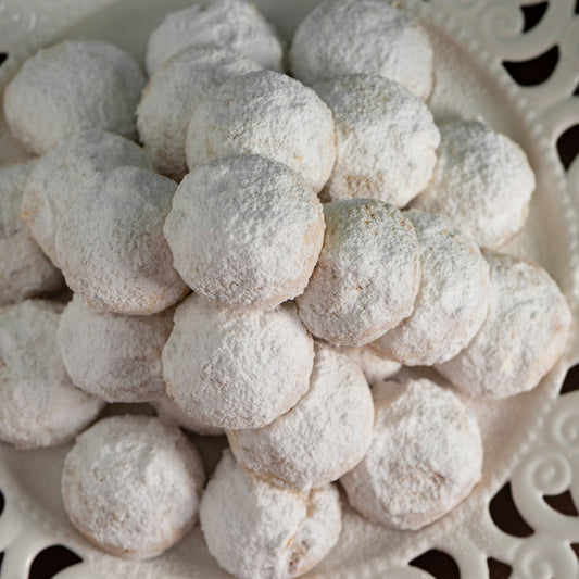 Gros plan de kourabiedes enrobés de sucre glace sur une assiette blanche ajourée