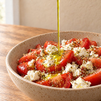 Huile d'olive extra vierge versée sur une salade de tomates et de feta