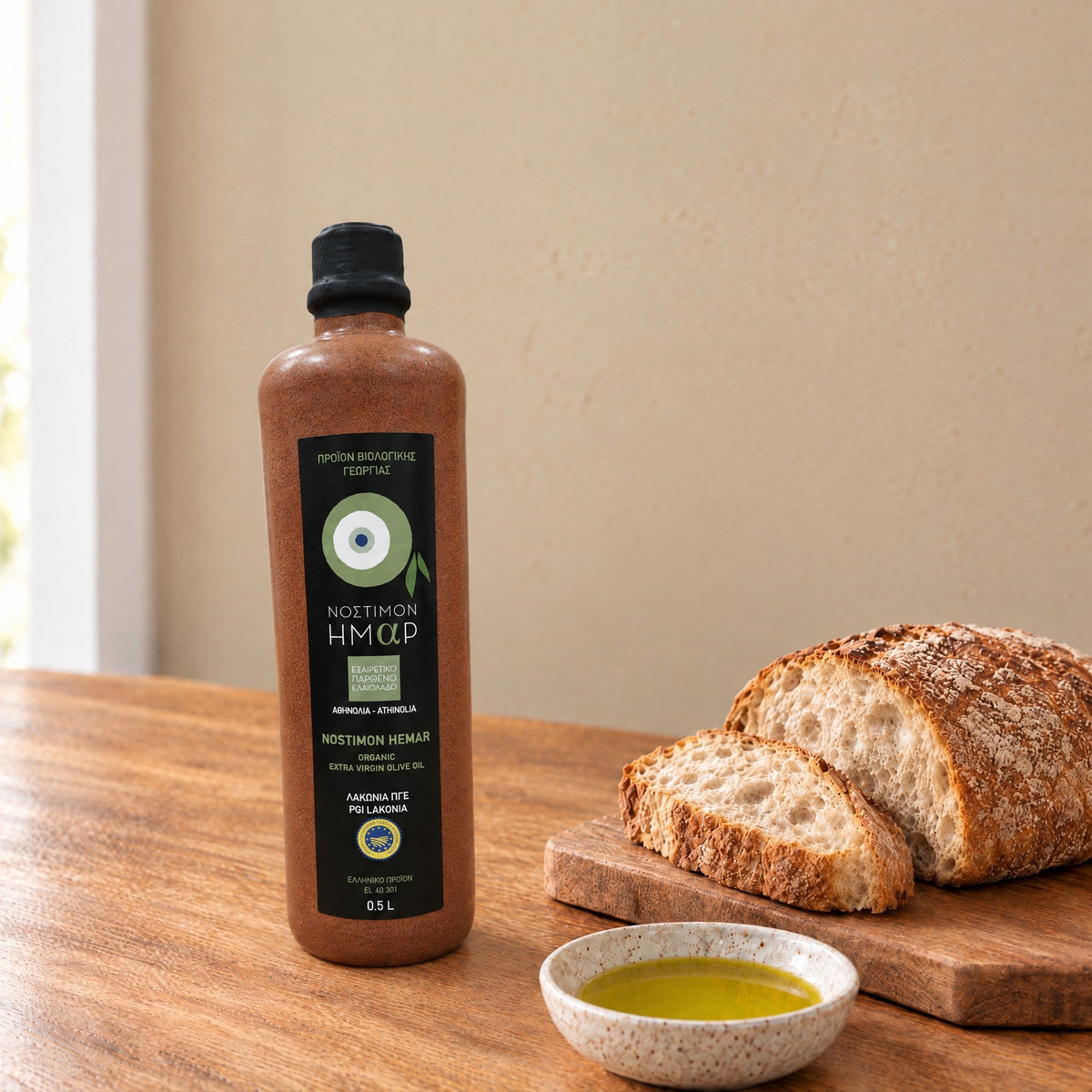 Nostimon Hemar organic Athinolia olive oil in a 500ml ceramic bottle beside bread and a dish of olive oil