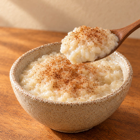 A wooden spoon lifting creamy rizogalo with cinnamon from a ceramic bowl
