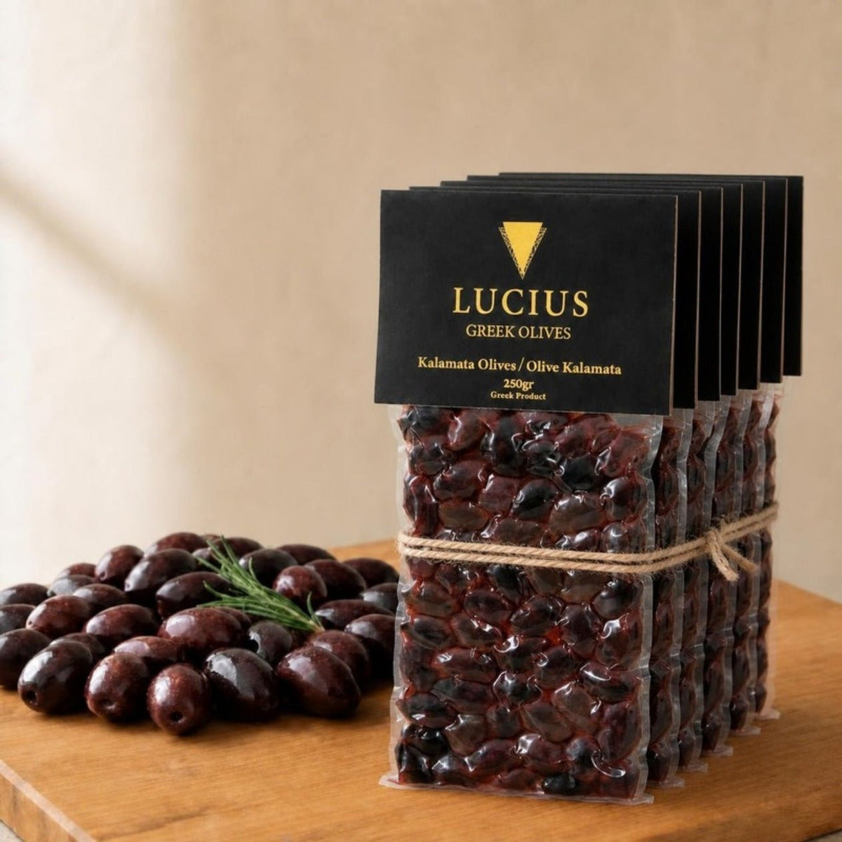 Six Lucius Kalamata olive pouches of 250g tied with twine beside a pile of olives on an oak board